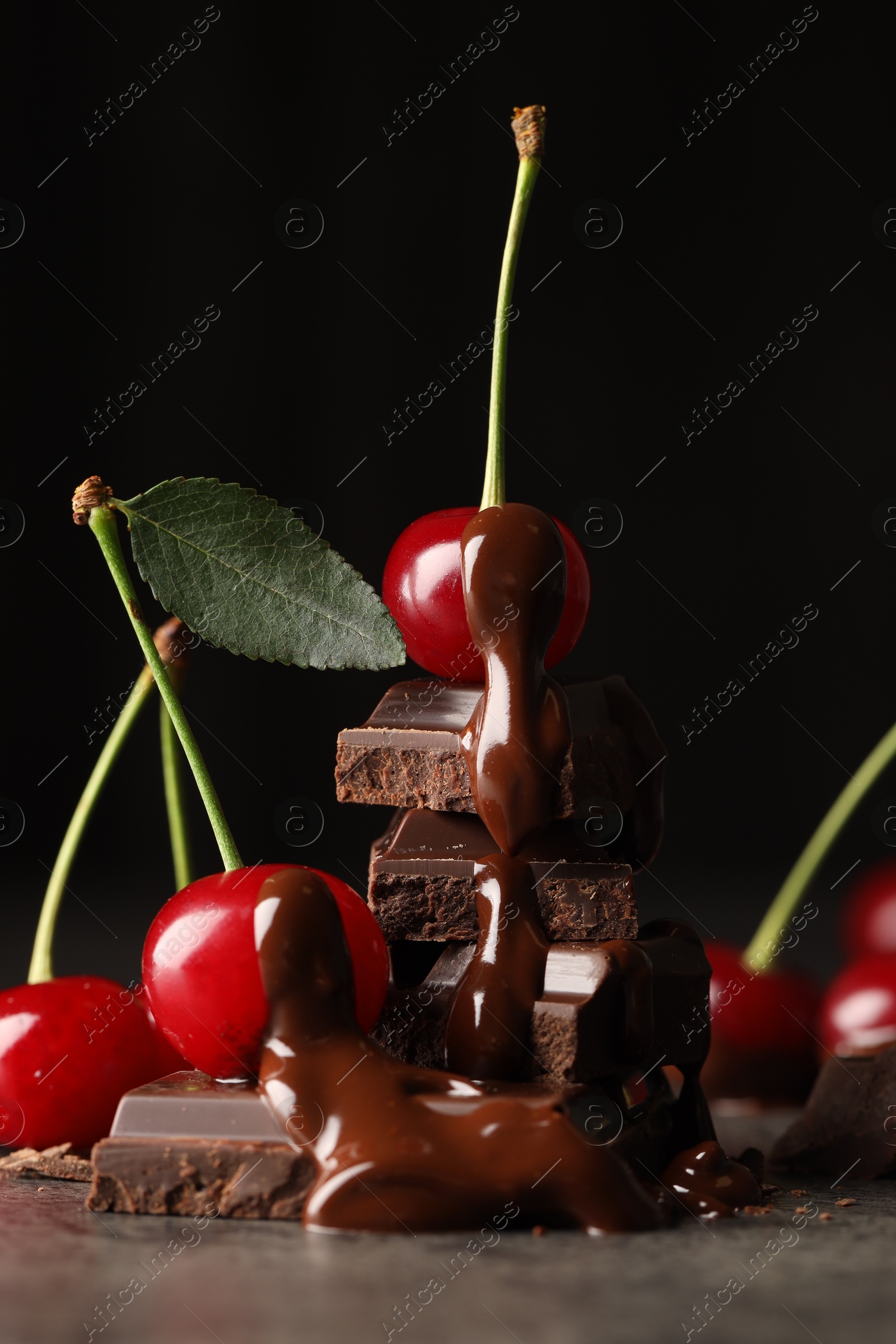 Photo of Fresh cherries with dark chocolate on grey textured table, closeup