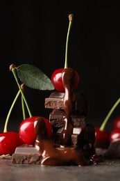 Photo of Fresh cherries with dark chocolate on grey textured table, closeup