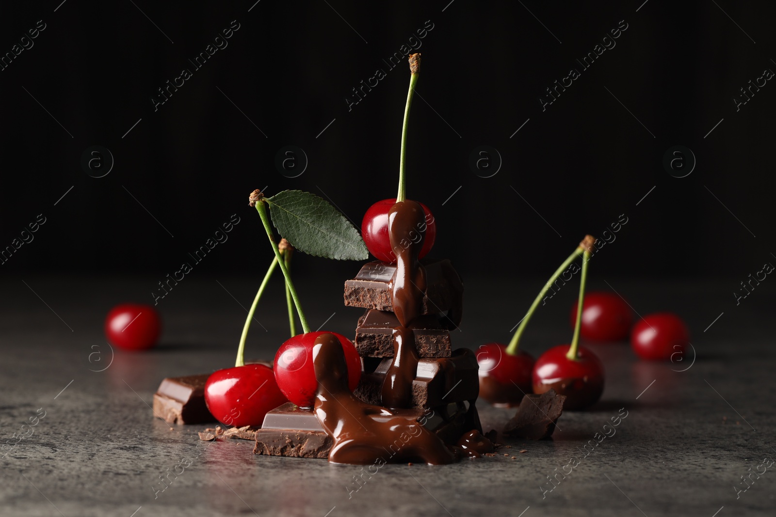 Photo of Fresh cherries with dark chocolate on grey textured table, closeup