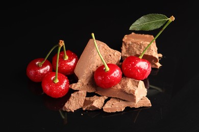 Photo of Fresh cherries with pieces of milk chocolate on black mirror surface