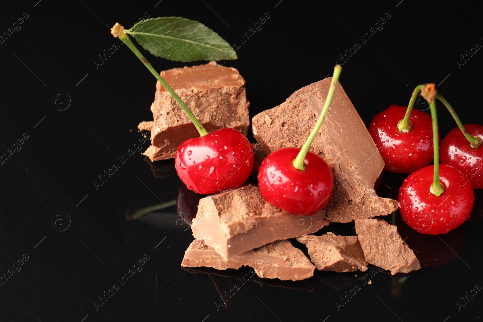 Photo of Fresh cherries with pieces of milk chocolate on black mirror surface