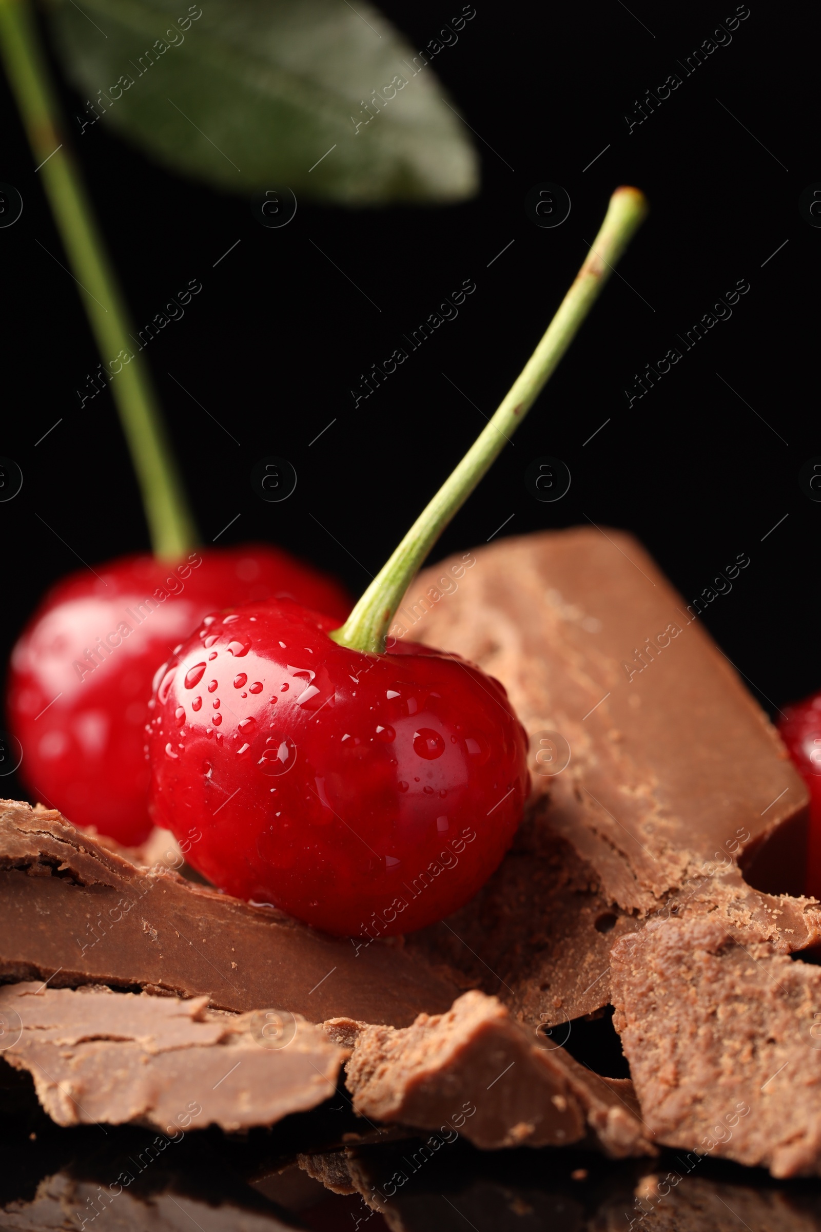 Photo of Fresh cherries with pieces of milk chocolate on black surface, closeup