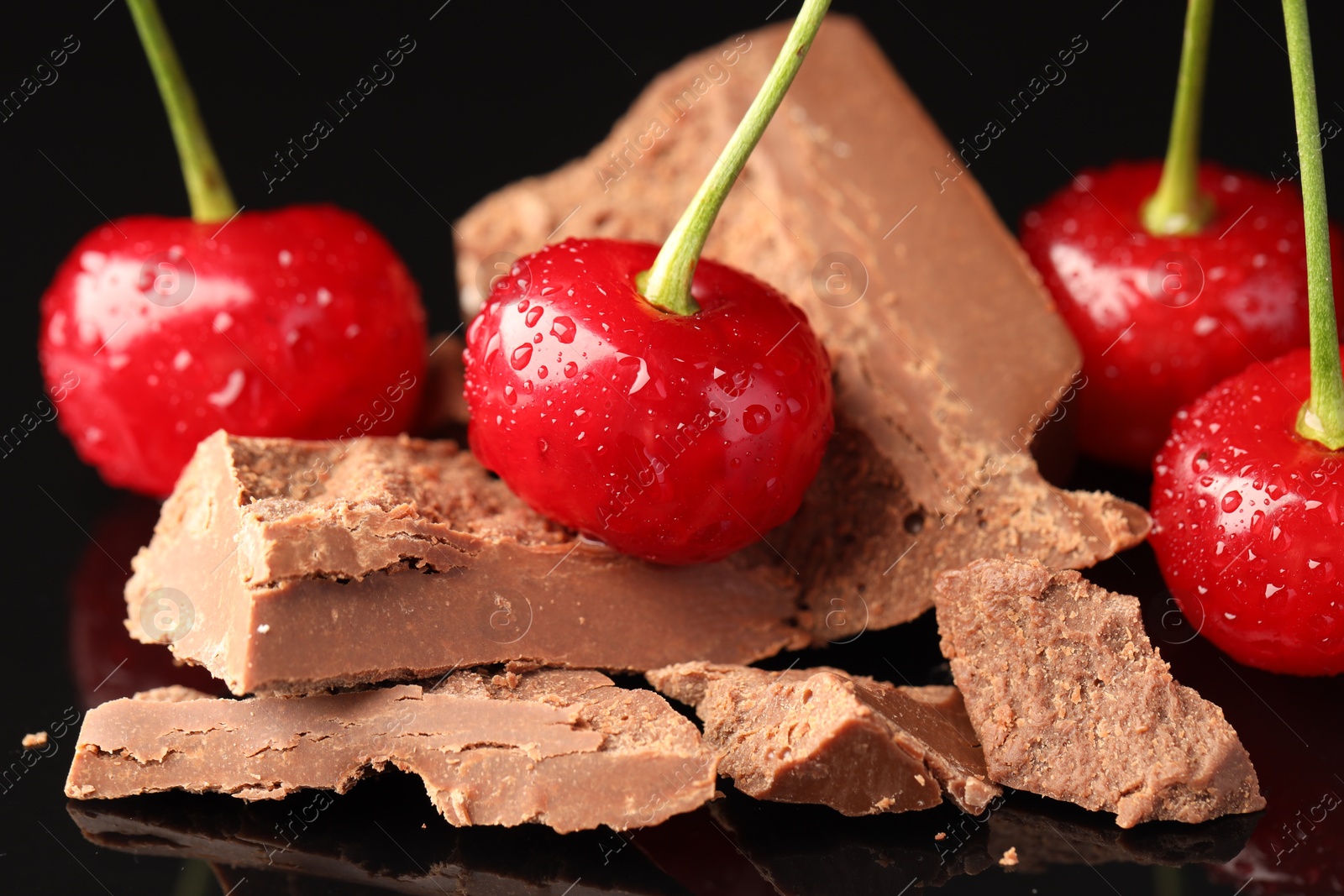 Photo of Fresh cherries with pieces of milk chocolate on black surface, closeup