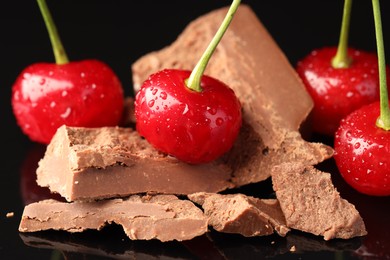 Fresh cherries with pieces of milk chocolate on black surface, closeup