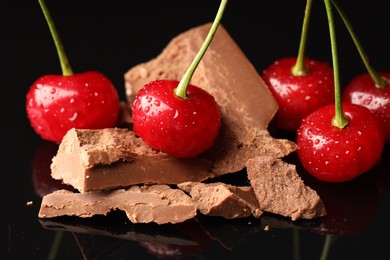 Fresh cherries with pieces of milk chocolate on black mirror surface, closeup