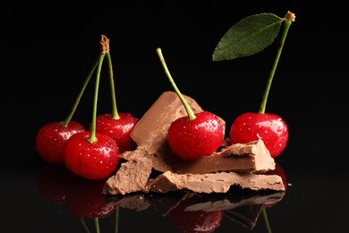 Photo of Fresh cherries with pieces of milk chocolate on black mirror surface, closeup