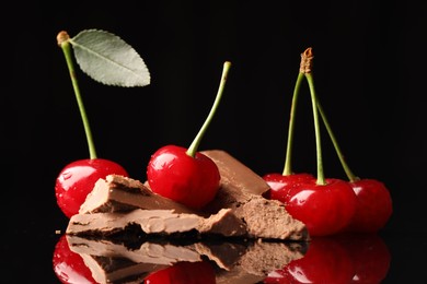 Photo of Fresh cherries with pieces of milk chocolate on black mirror surface, closeup