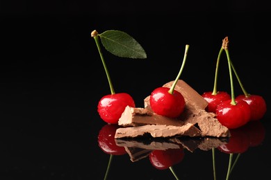 Photo of Fresh cherries with pieces of milk chocolate on black mirror surface, space for text