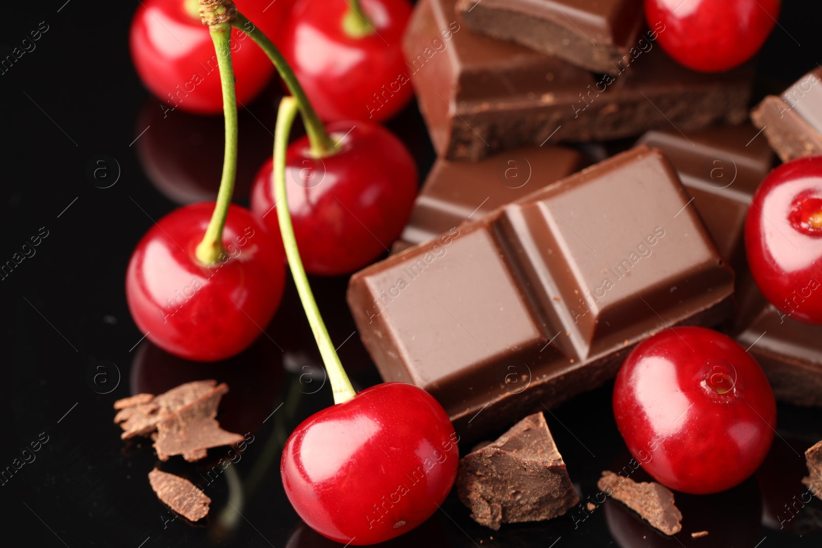 Photo of Fresh cherries with pieces of milk chocolate on black mirror surface, closeup