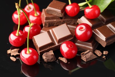 Photo of Fresh cherries with pieces of milk chocolate on black mirror surface, closeup