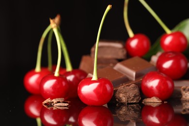 Photo of Fresh cherries with pieces of milk chocolate on black mirror surface, closeup