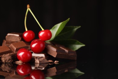 Photo of Fresh cherries with pieces of milk chocolate and green leaves on black mirror surface, closeup. Space for text