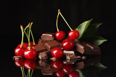 Photo of Fresh cherries with pieces of milk chocolate and green leaves on black mirror surface