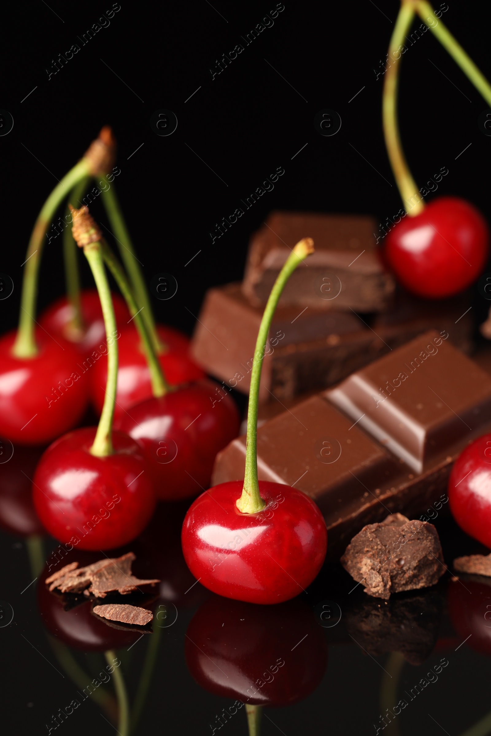 Photo of Fresh cherries with pieces of milk chocolate on black mirror surface, closeup