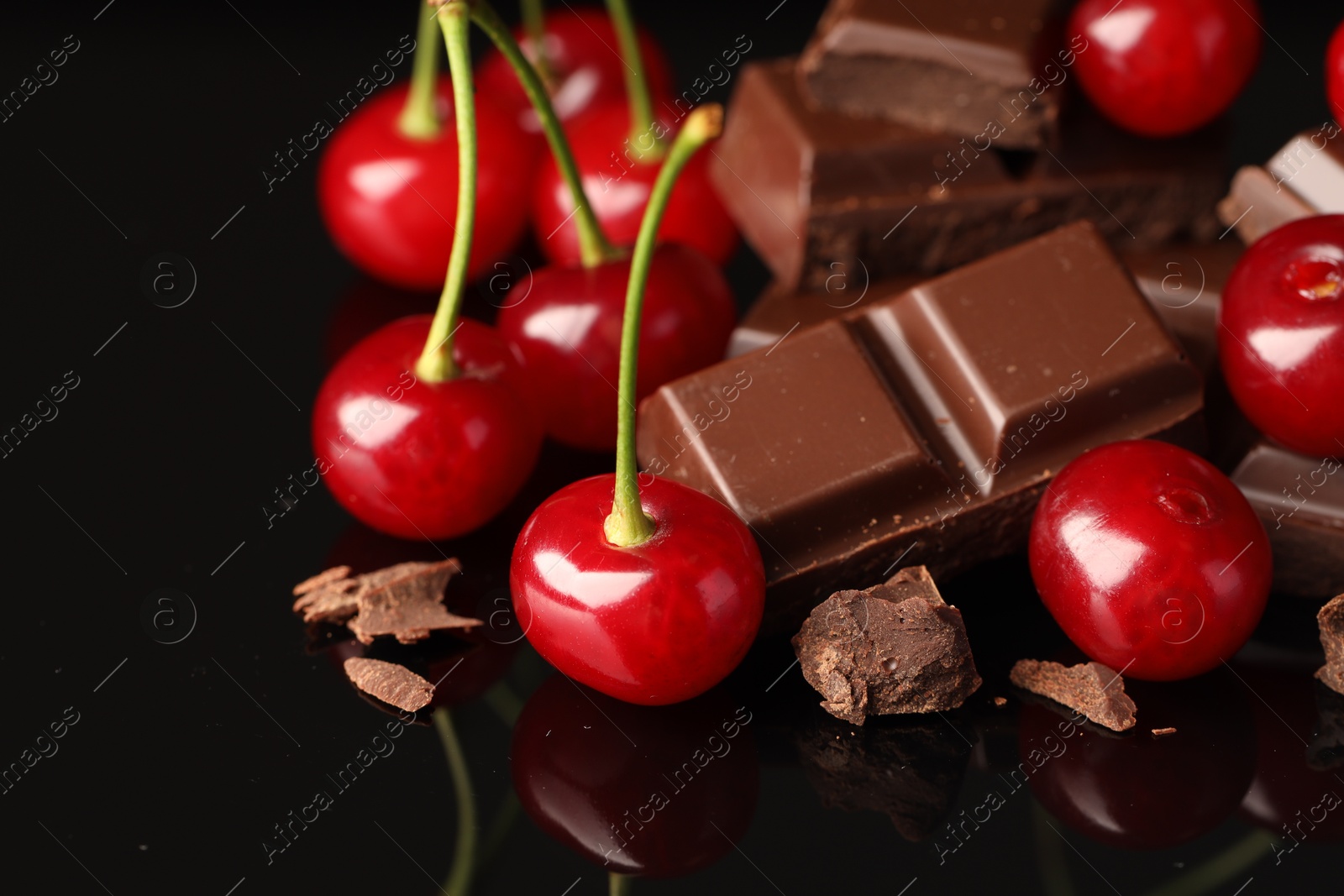 Photo of Fresh cherries with pieces of milk chocolate on black mirror surface, closeup