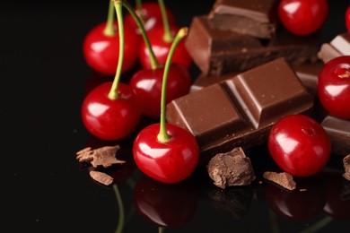 Photo of Fresh cherries with pieces of milk chocolate on black mirror surface, closeup