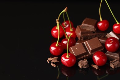 Fresh cherries with pieces of milk chocolate on black mirror surface, space for text