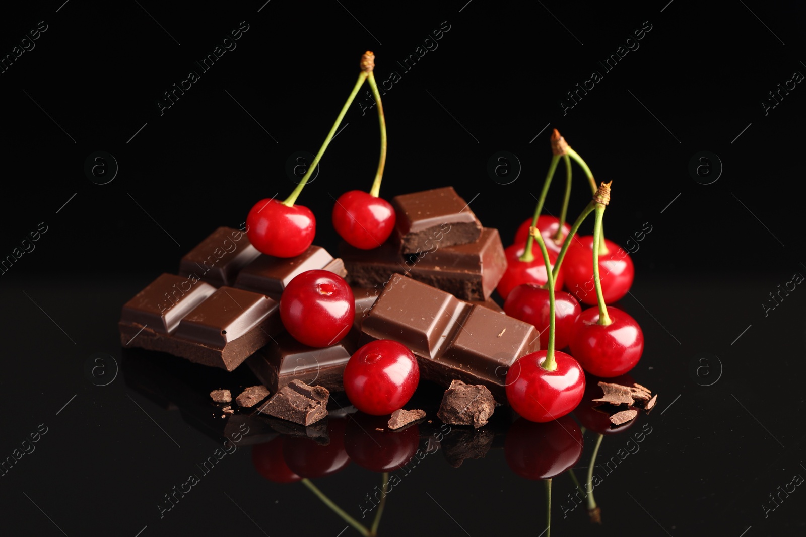 Photo of Fresh cherries with pieces of milk chocolate on black mirror surface