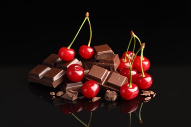 Photo of Fresh cherries with pieces of milk chocolate on black mirror surface