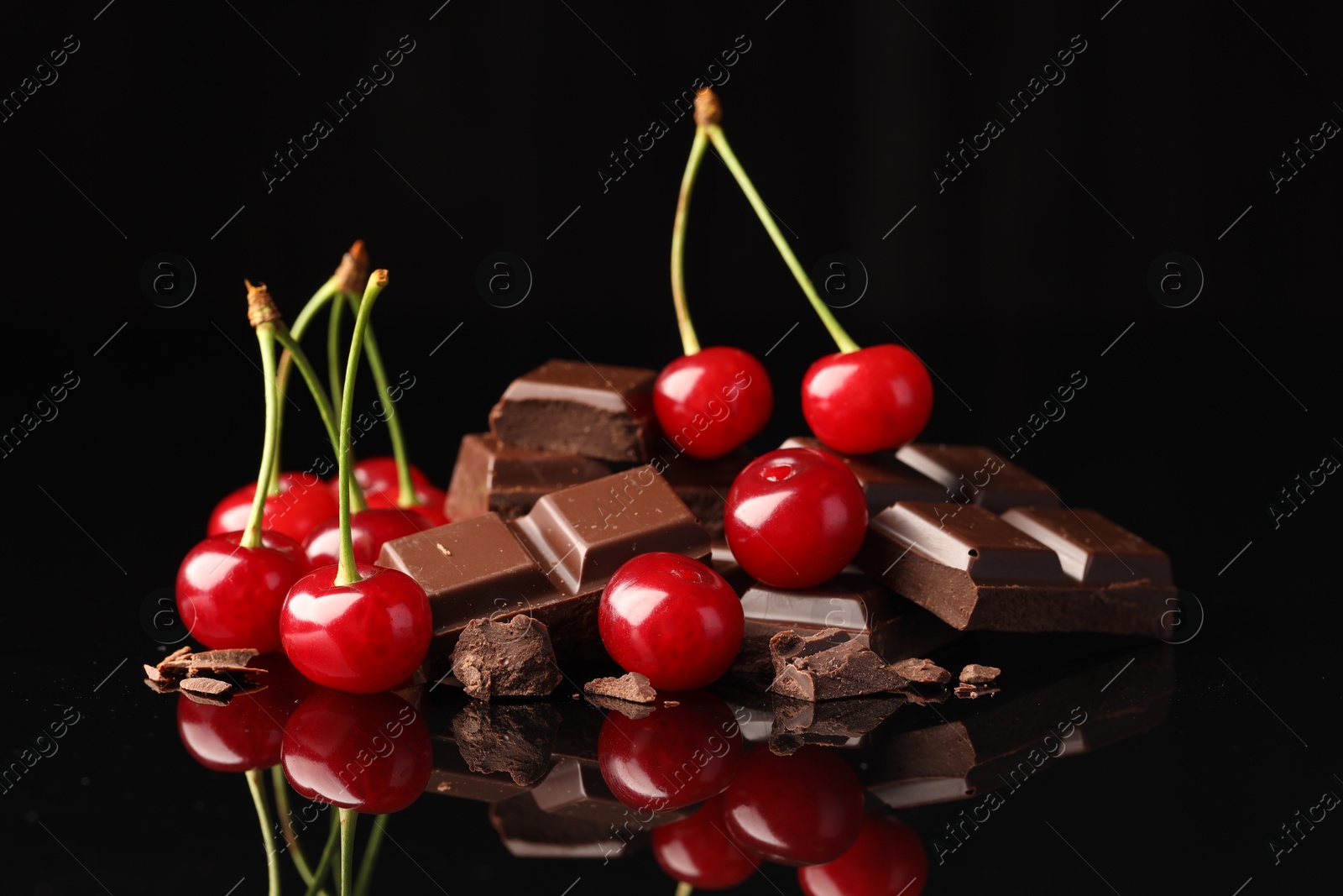 Photo of Fresh cherries with pieces of milk chocolate on black mirror surface