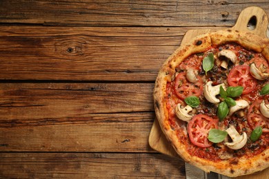 Photo of Tasty pizza with basil, mushrooms and tomato on wooden table, top view. Space for text