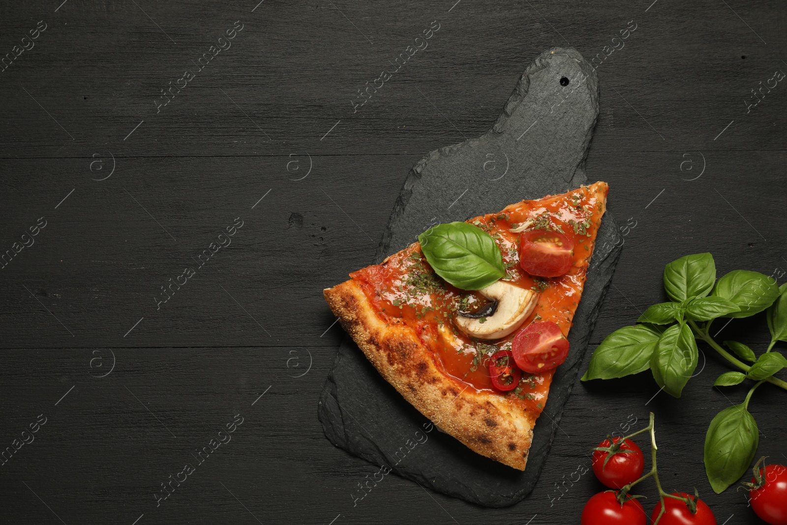 Photo of Piece of tasty pizza with basil, mushroom and tomato on black wooden table, flat lay. Space for text