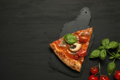 Piece of tasty pizza with basil, mushroom and tomato on black wooden table, flat lay. Space for text