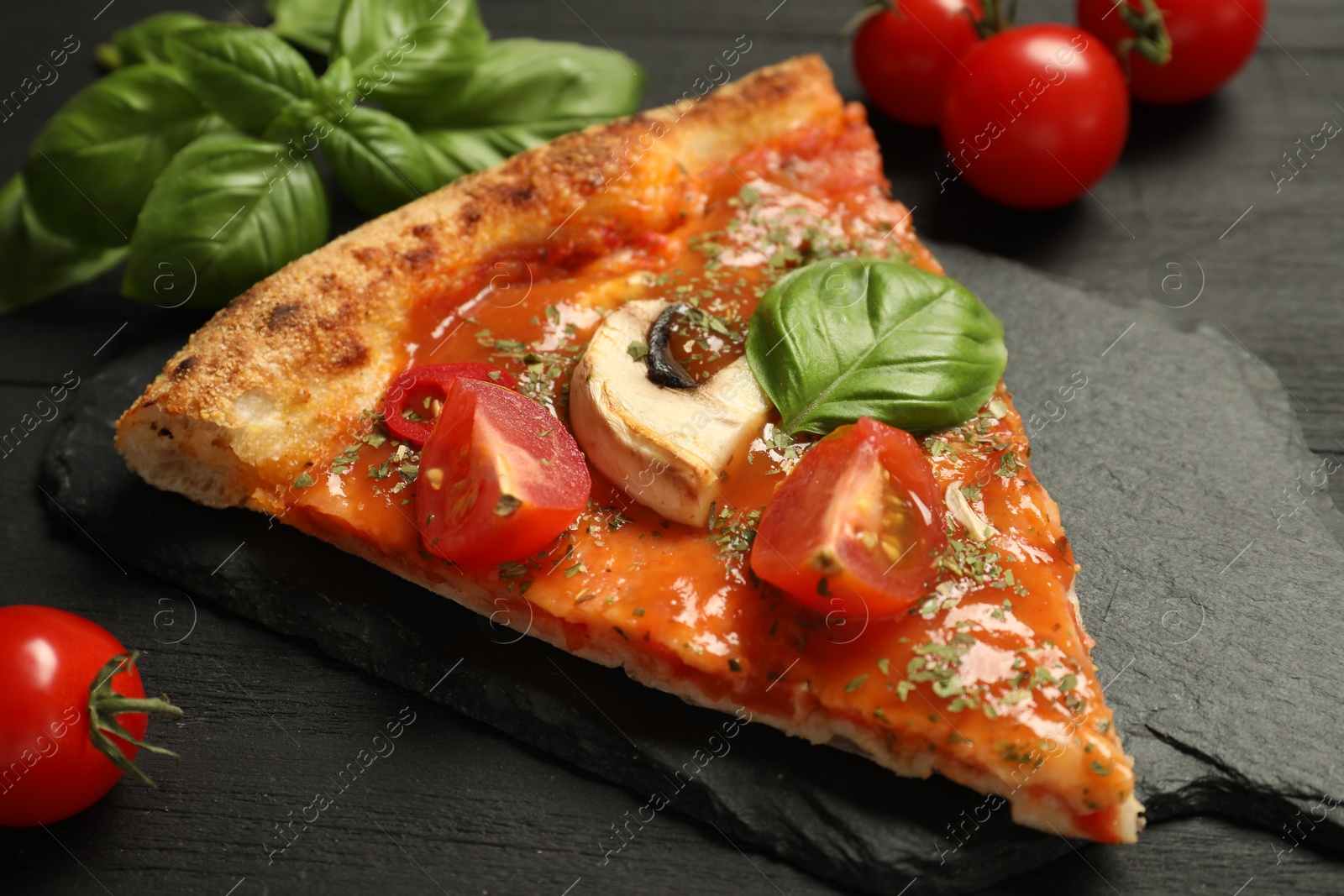 Photo of Piece of tasty pizza with basil, mushroom and tomato on black wooden table, closeup