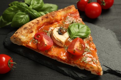 Piece of tasty pizza with basil, mushroom and tomato on black wooden table, closeup