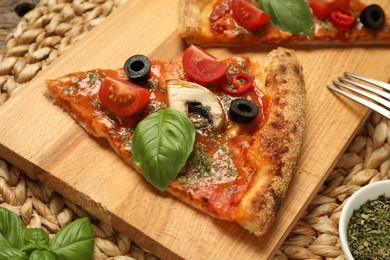 Photo of Piece of tasty pizza with basil, olives and tomato on wicker mat, closeup