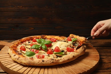 Woman taking piece of tasty pizza with melted cheese at wooden table, closeup