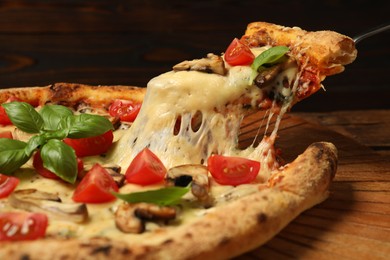 Photo of Taking piece of tasty pizza with melted cheese at wooden table, closeup