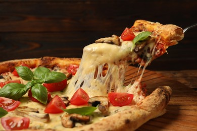 Photo of Taking piece of tasty pizza with melted cheese at wooden table, closeup