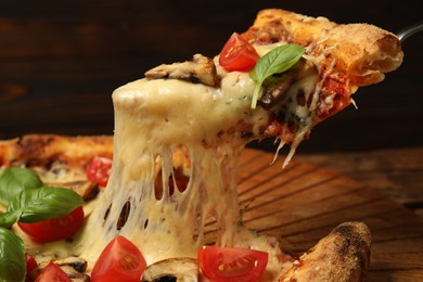 Photo of Taking piece of tasty pizza with melted cheese at wooden table, closeup