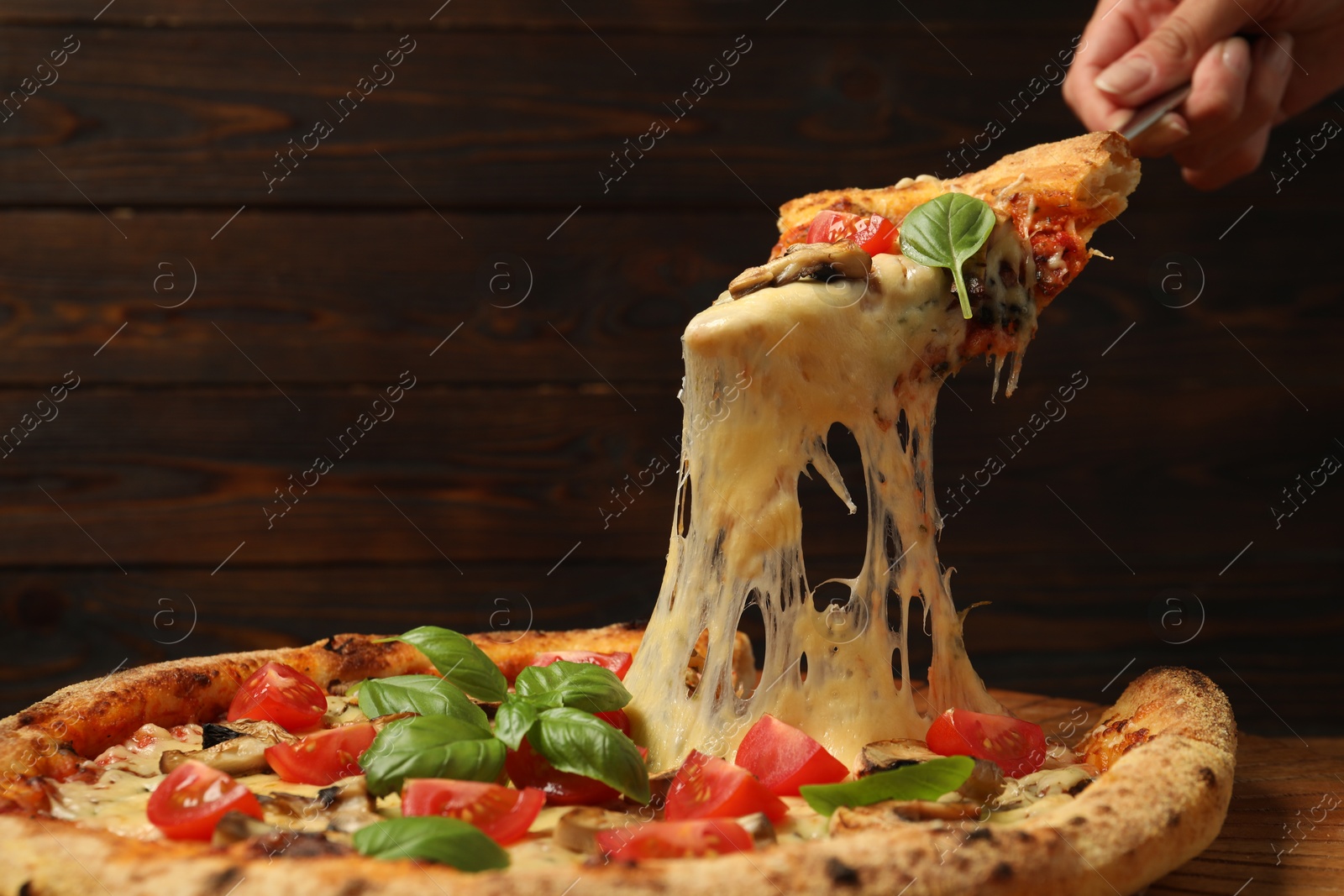 Photo of Woman taking piece of tasty pizza with melted cheese at wooden table, closeup