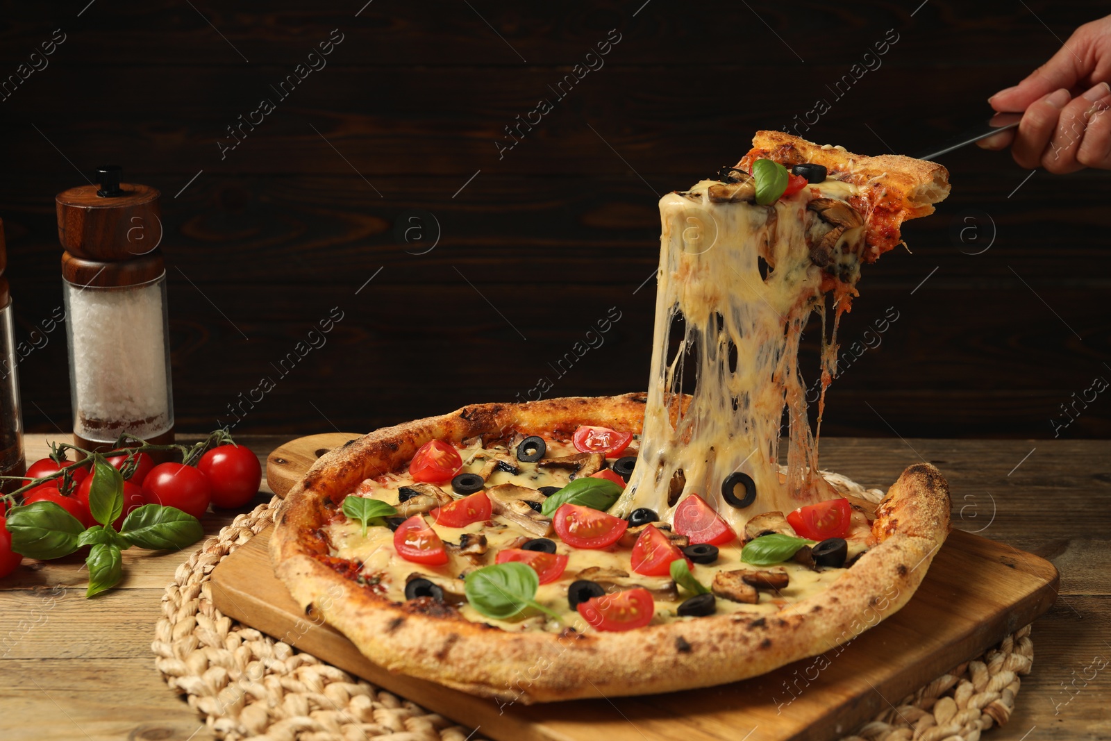 Photo of Woman taking piece of tasty pizza with melted cheese at wooden table, closeup