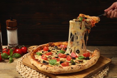 Photo of Woman taking piece of tasty pizza with melted cheese at wooden table, closeup