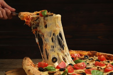 Photo of Woman taking piece of tasty pizza with melted cheese at wooden table, closeup