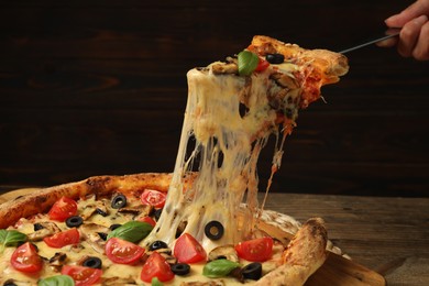 Woman taking piece of tasty pizza with melted cheese at wooden table, closeup