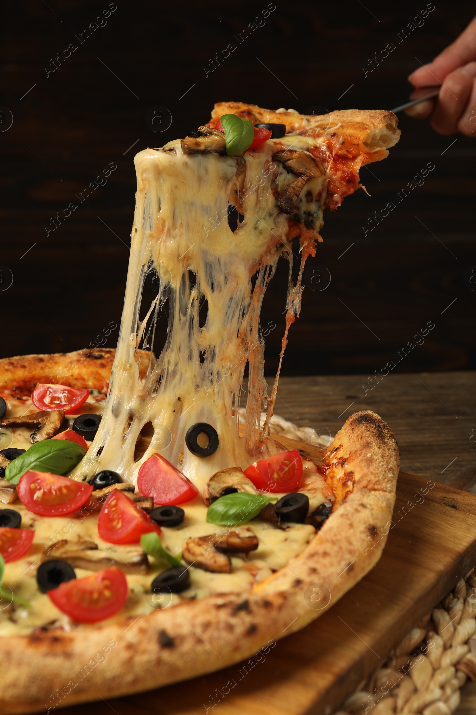 Photo of Woman taking piece of tasty pizza with melted cheese at wooden table, closeup