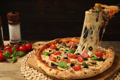 Photo of Taking piece of tasty pizza with melted cheese at wooden table, closeup