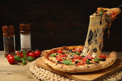 Taking piece of tasty pizza with melted cheese at wooden table, closeup