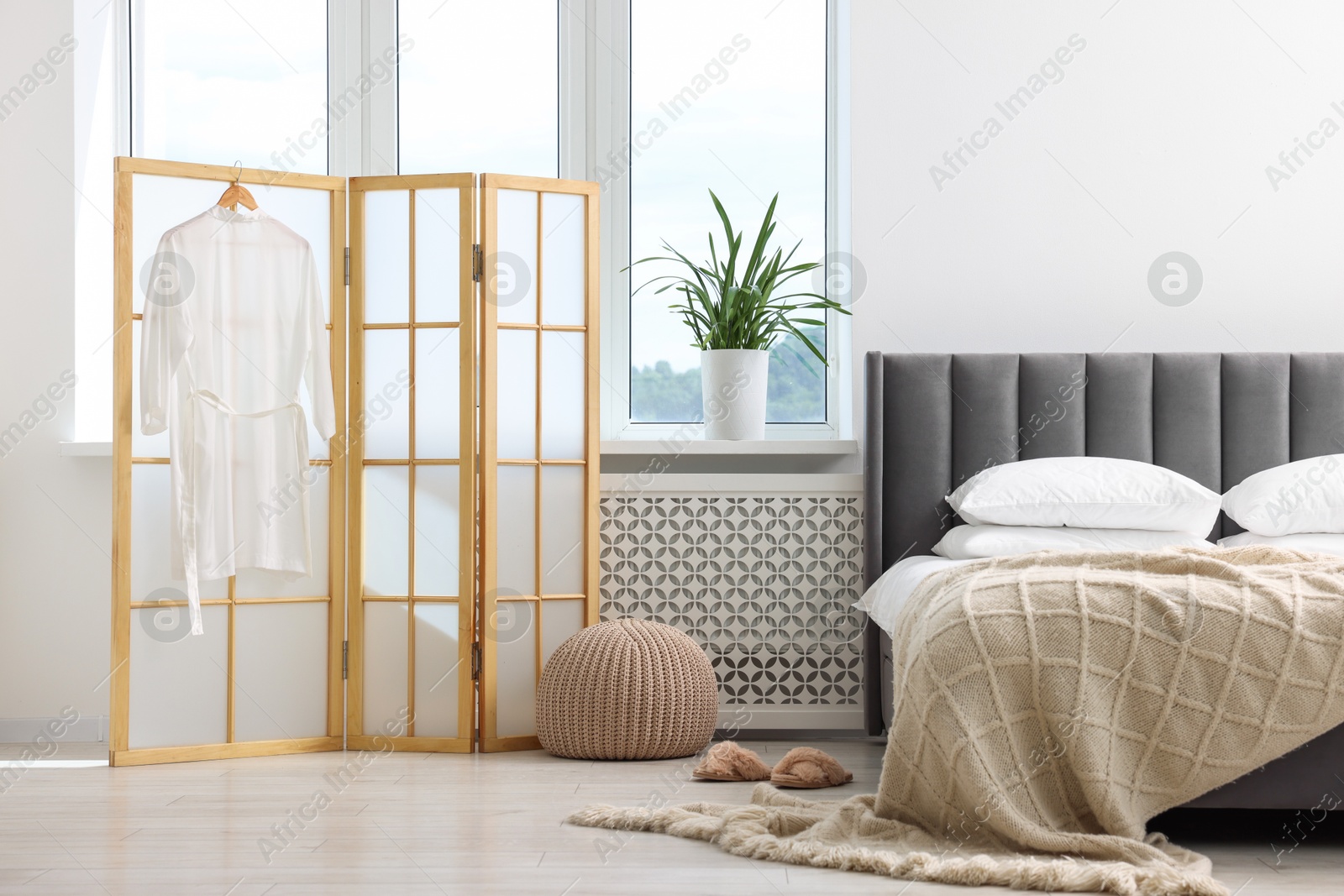 Photo of Folding screen, pouffe, bed and houseplant in bedroom