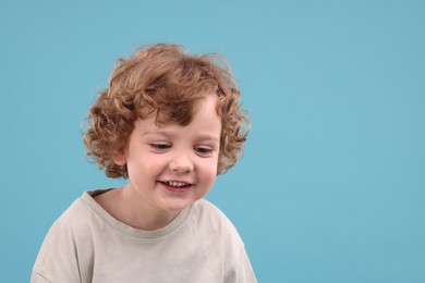 Portrait of cute little boy on light blue background, space for text