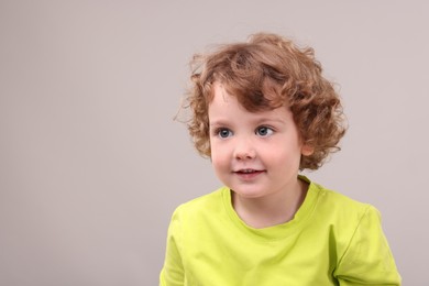 Portrait of cute little boy on grey background, space for text