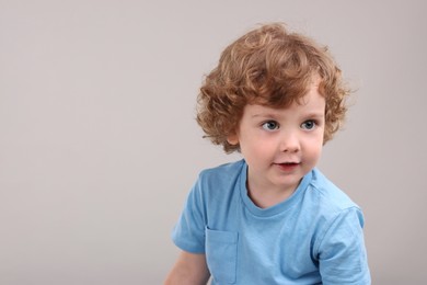 Portrait of cute little boy on grey background, space for text