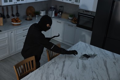 Photo of Thief wearing balaclava with crowbar stealing wallet and money in foreign house. Burglary