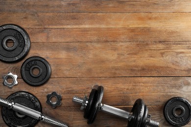 Barbell and parts of one on wooden floor, flat lay. Space for text