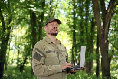 Forester with laptop examining plants in forest