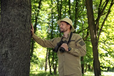 Forester with binoculars examining tree in forest